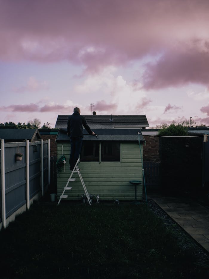 Crafting Captivating Headlines: Your awesome post title goes here A man fixing the roof of a small shed in a backyard at dusk with a dramatic sky.