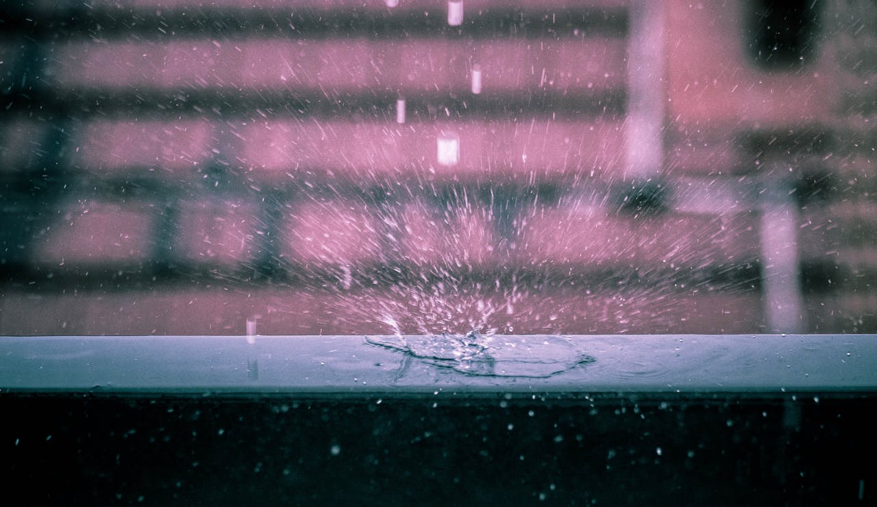 Dramatic capture of a rain droplet splashing on a surface with blurred urban background.