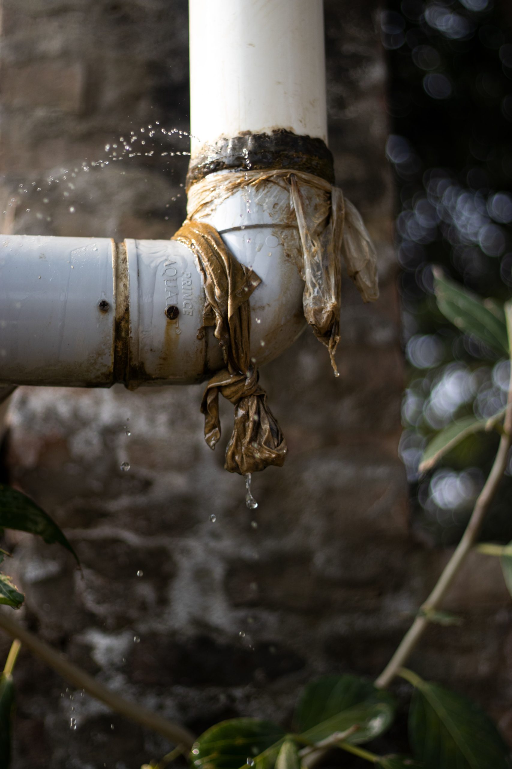 Pipe & Penetration Leaks in Singapore – Causes, Diagnosis and How to Tell the Difference Close-up of a leaking plastic pipe outdoors with water dripping, showing wear and tear.